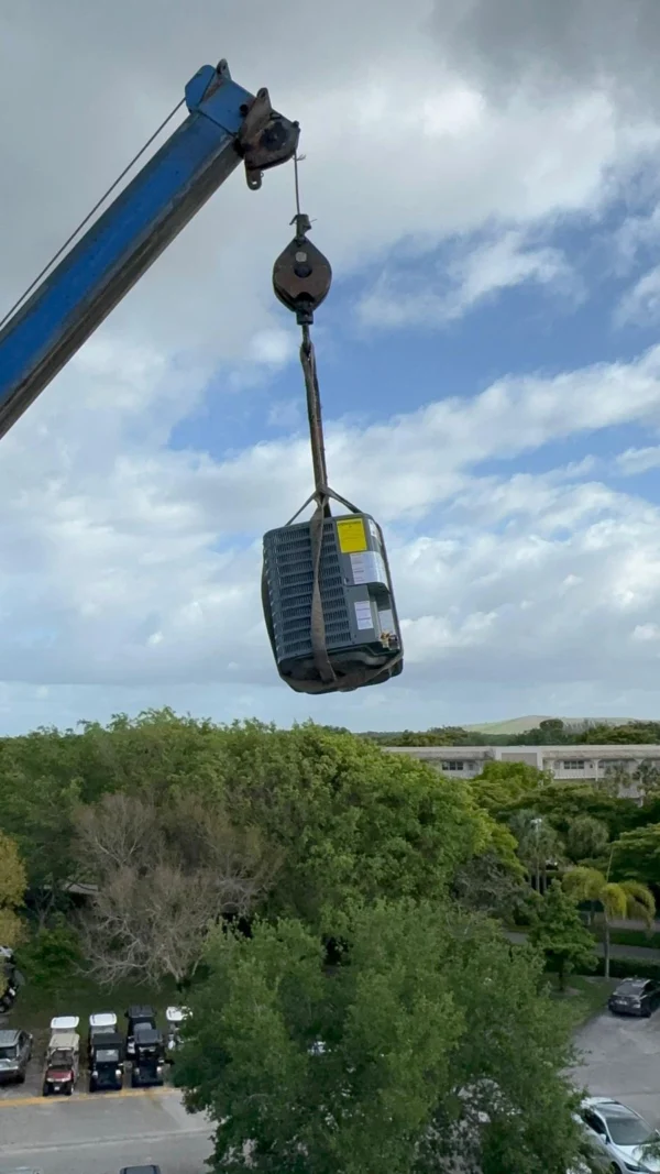 Crane lifting a new AC condenser unit into place