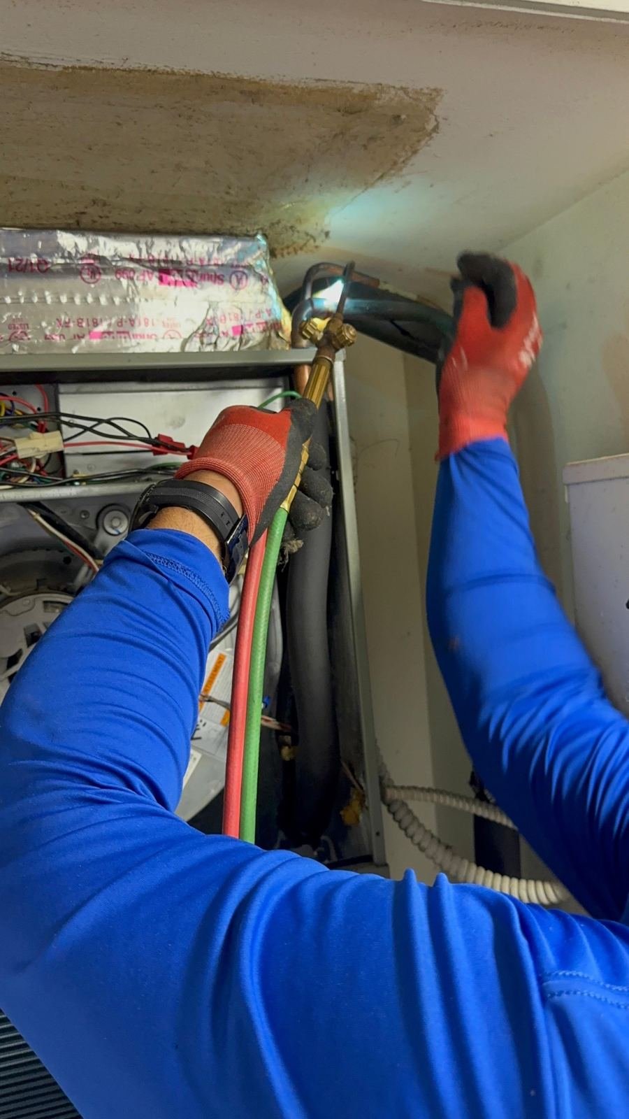 Technician brazing refrigerant lines in a tight overhead space
