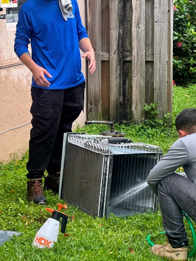 Technicians cleaning an AC coil with a spray hose